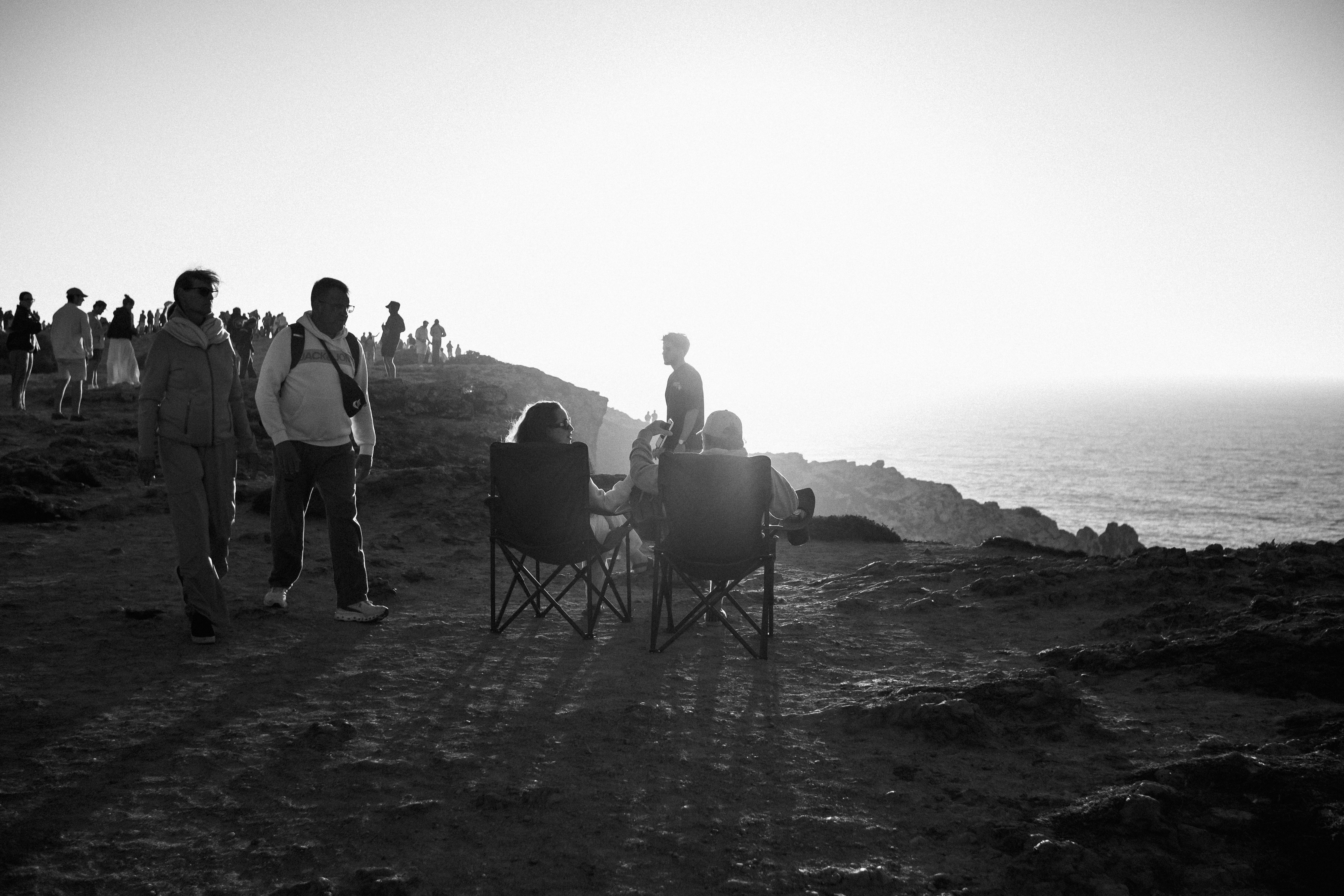 People sitting on chairs overlooking the ocean at sunset.