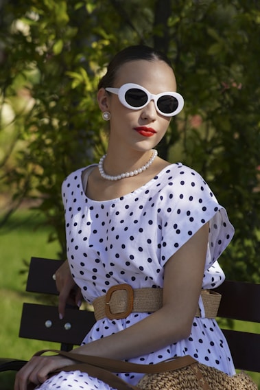 Woman in polka dots and sunglasses sits on bench