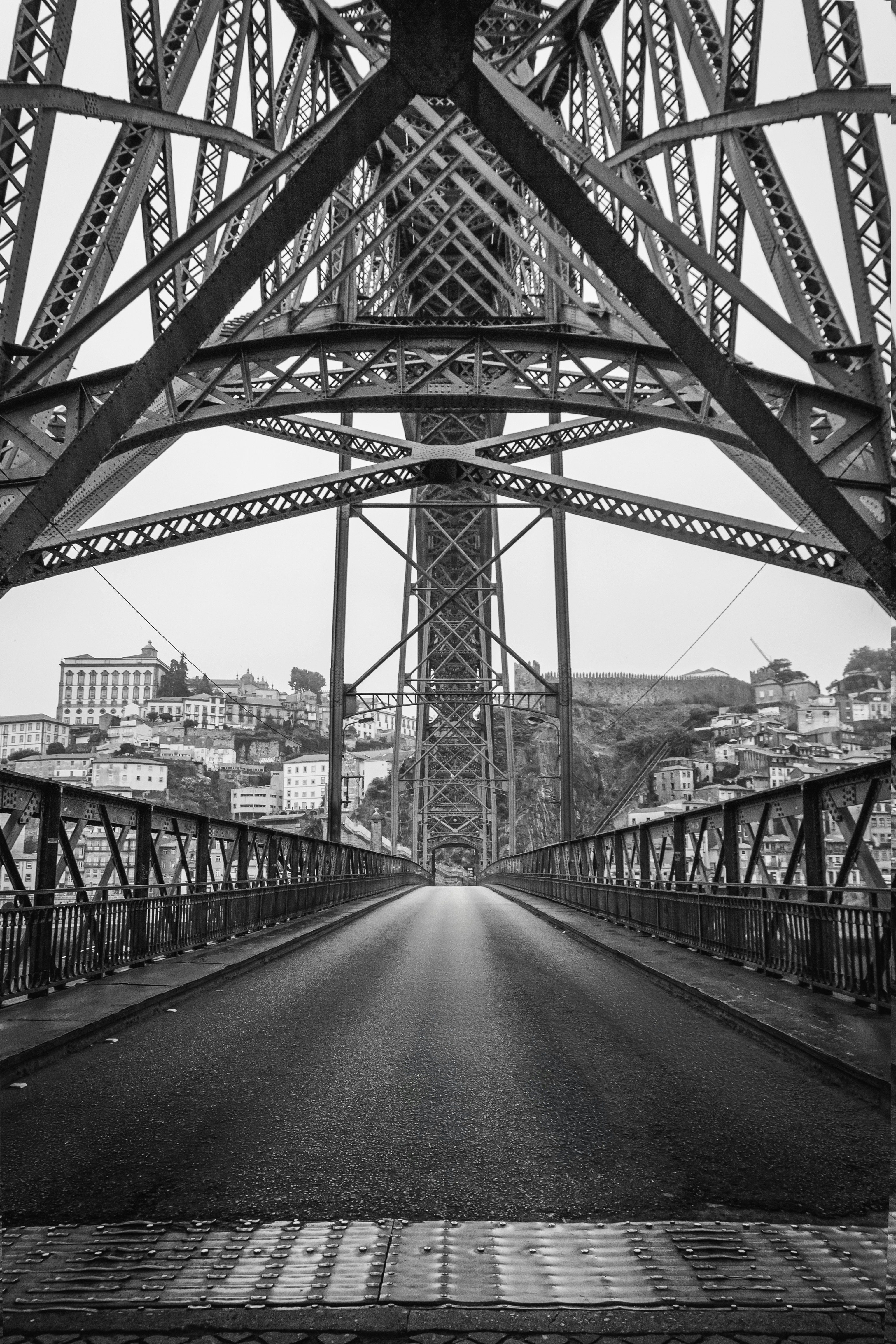 A grayscale view of a metal bridge with city buildings beyond.
