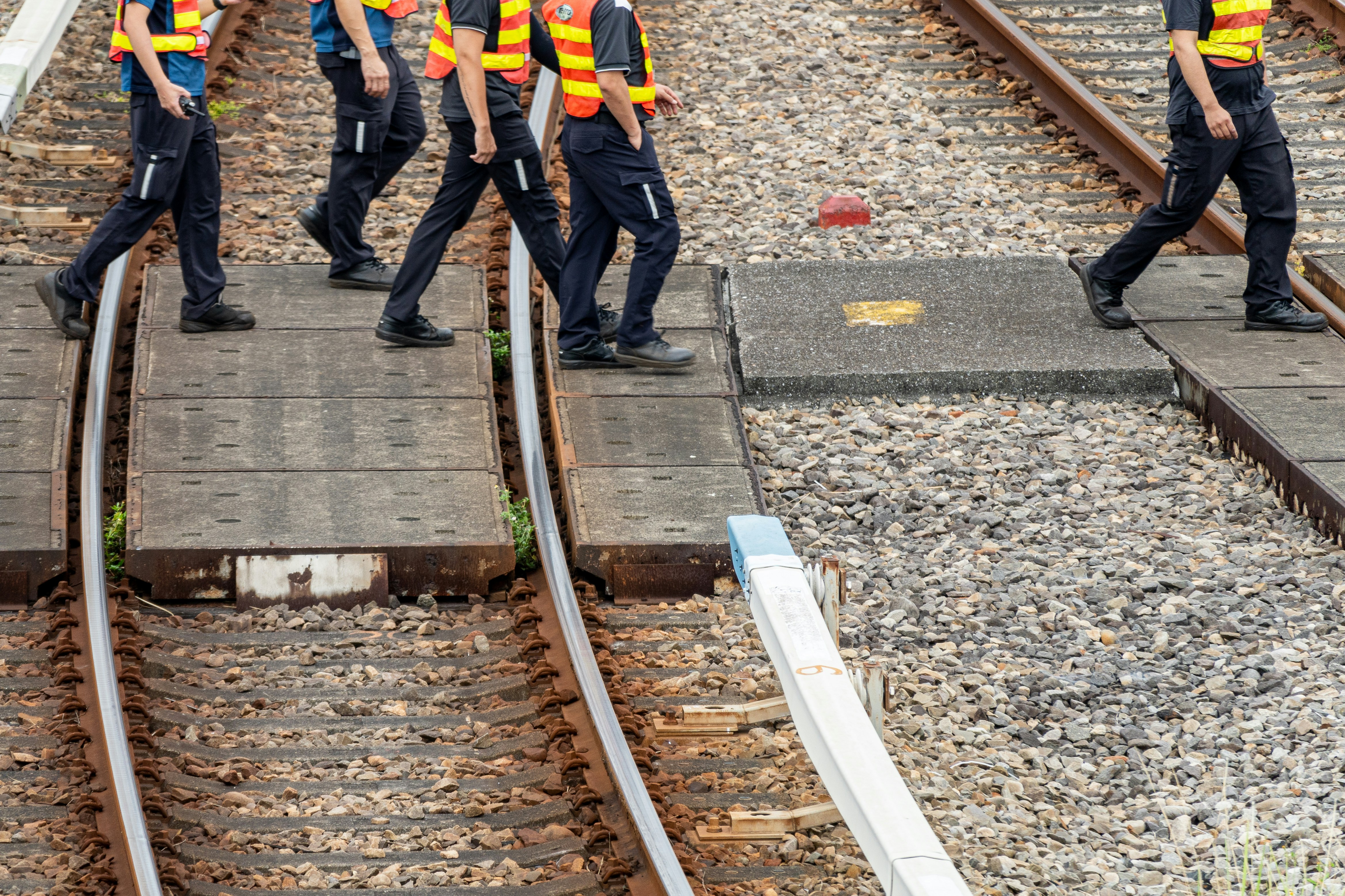 People in safety vests walk across train tracks.