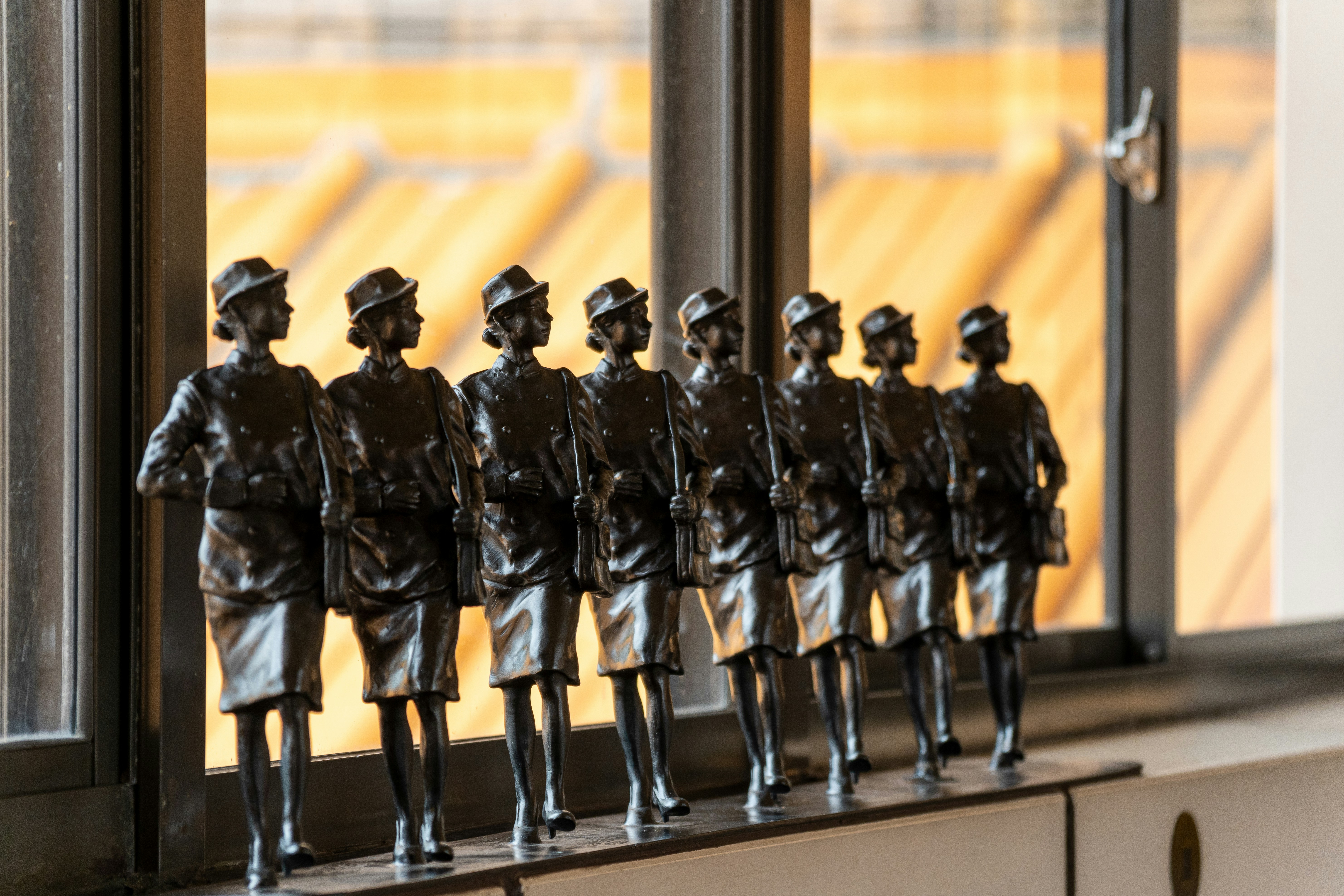 Eight dark bronze female figures stand in a line.