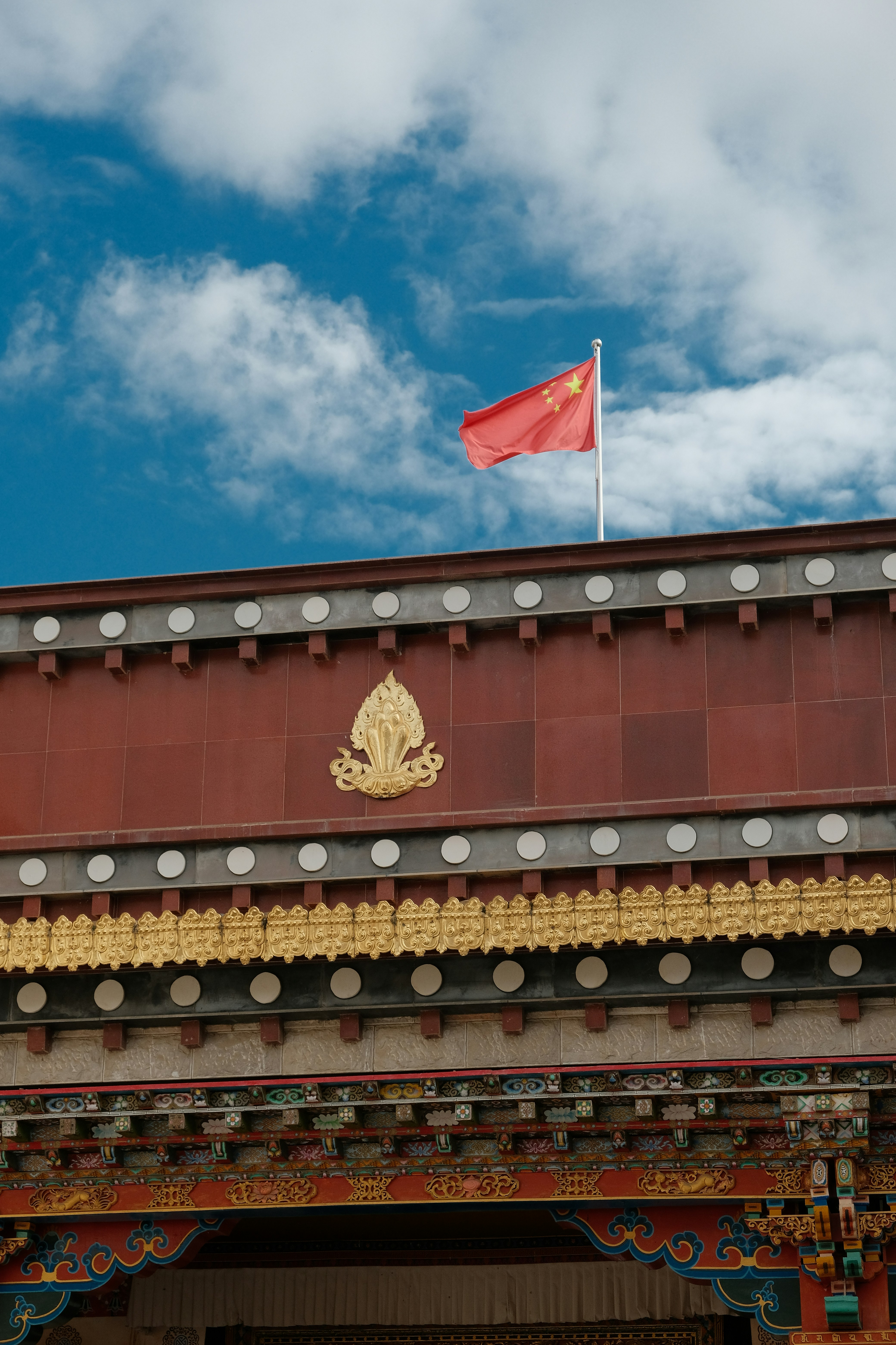 Red chinese flag flies on building under blue sky.