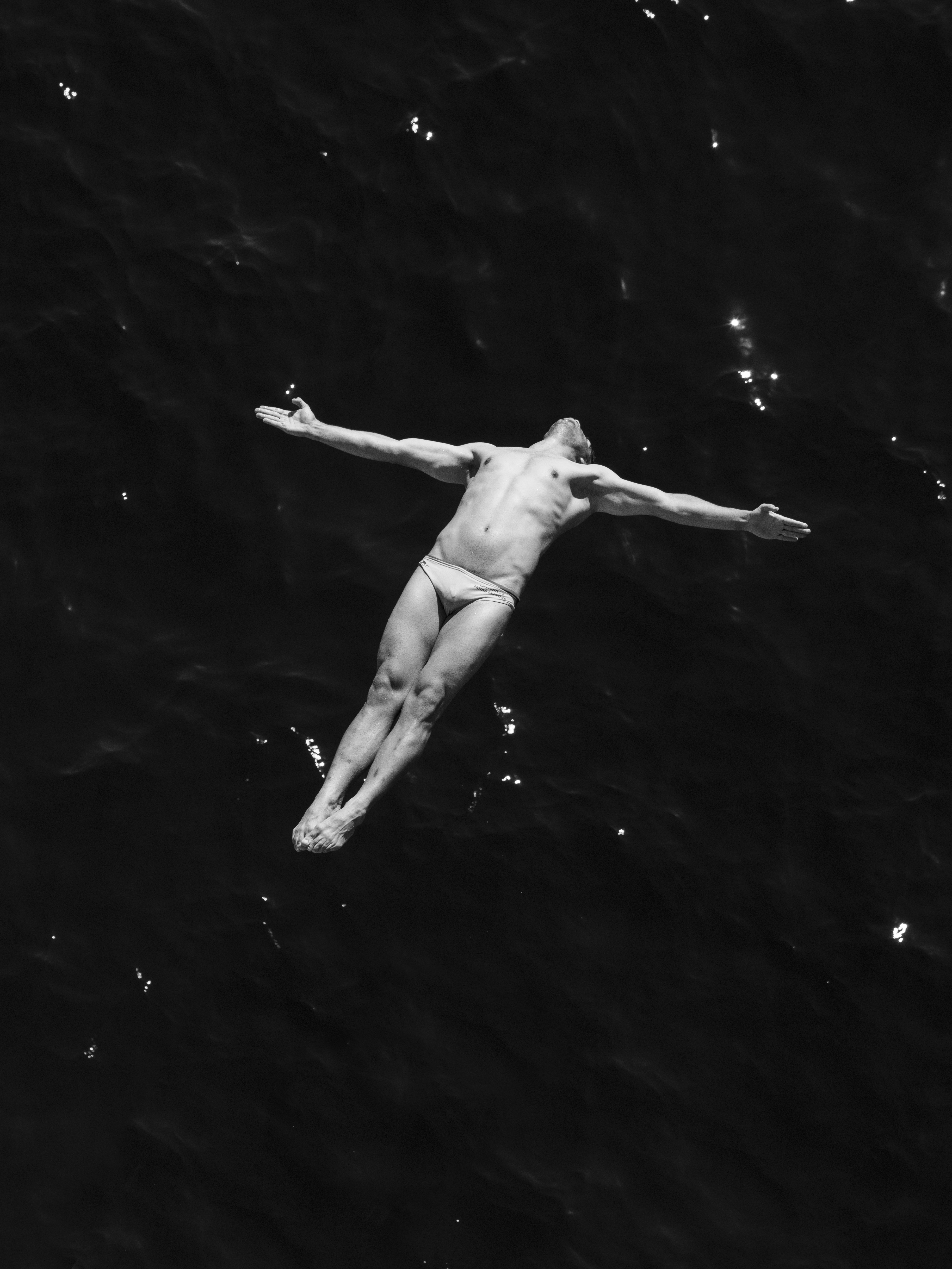 Man diving into dark water with arms outstretched