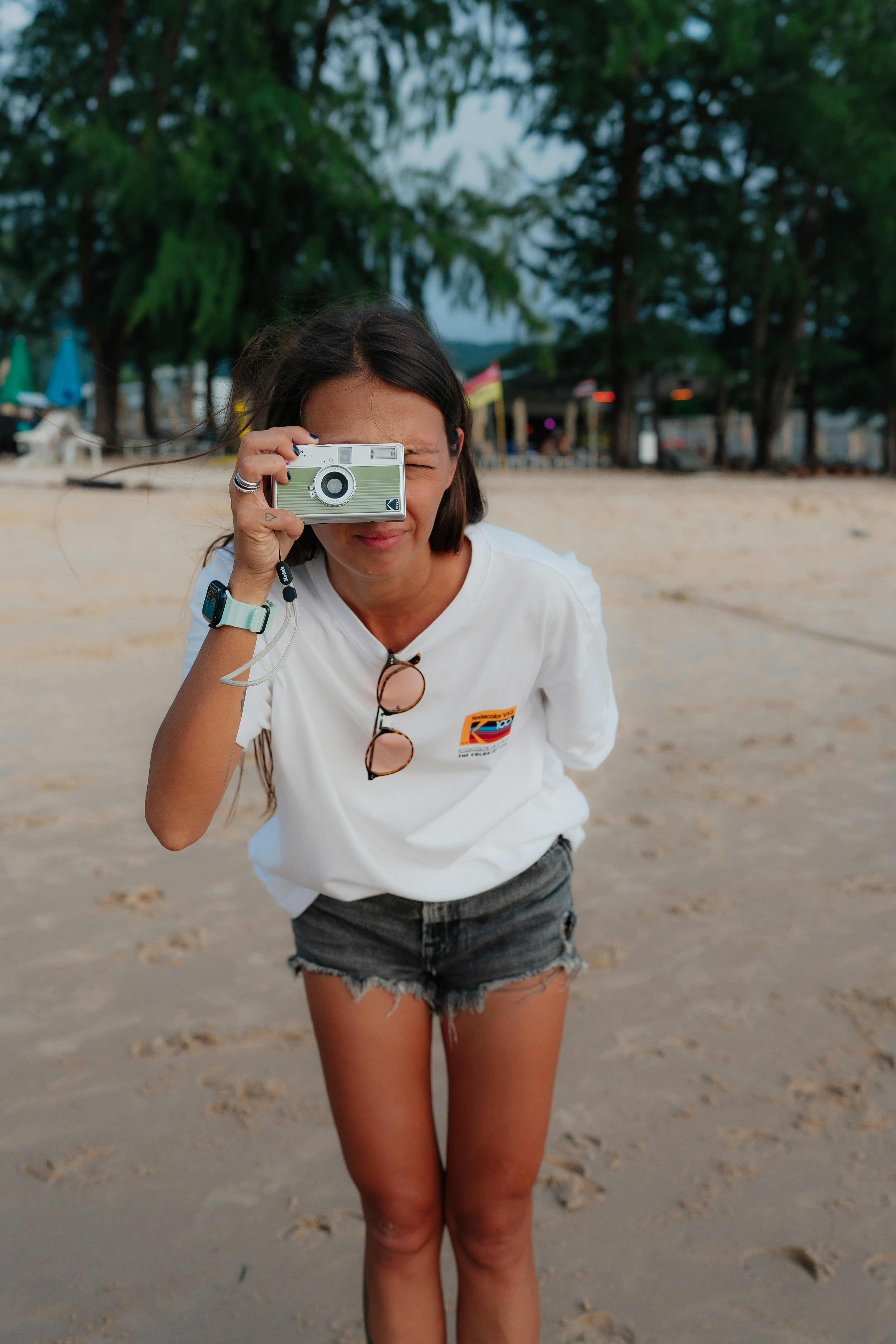Wanita memegang kamera di pantai berpasir