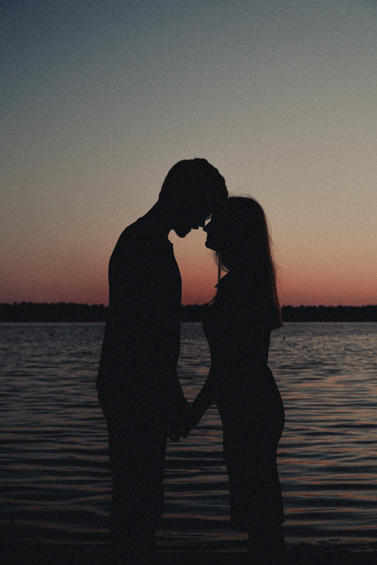A couple holding hands by the water at sunset