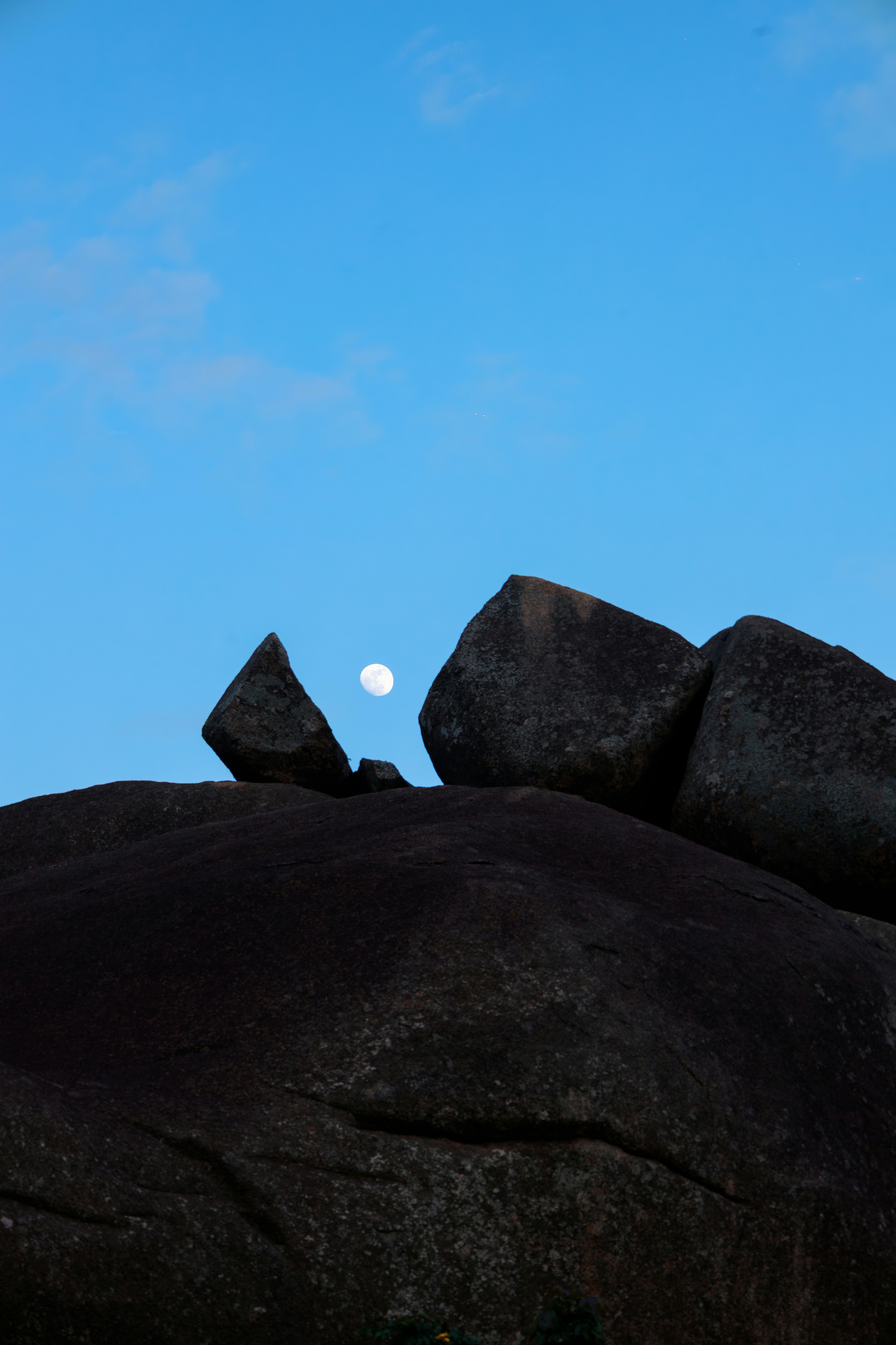 Full moon visible behind dark, large rocks.