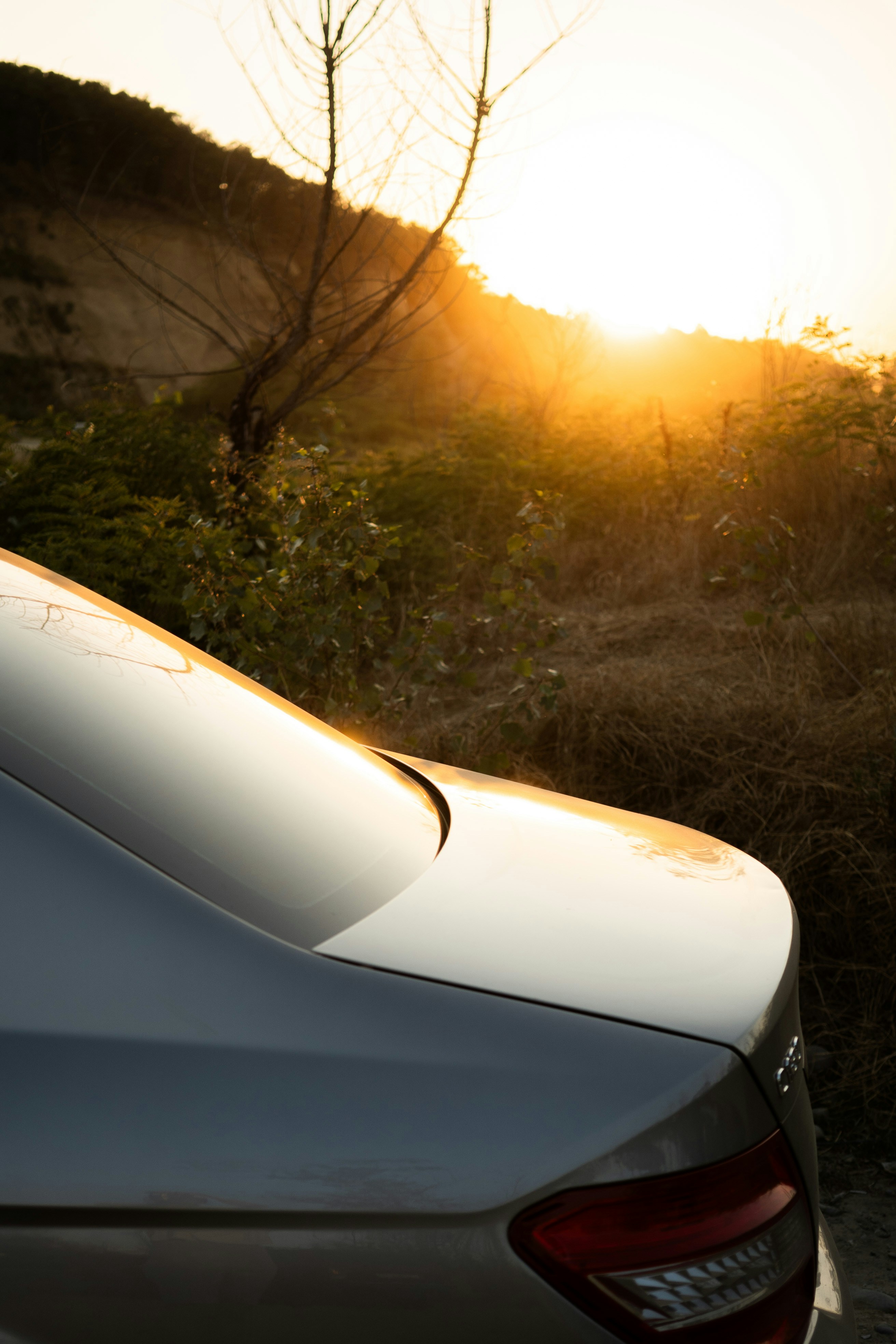 Auto d'argento parcheggiata vicino a una collina al tramonto