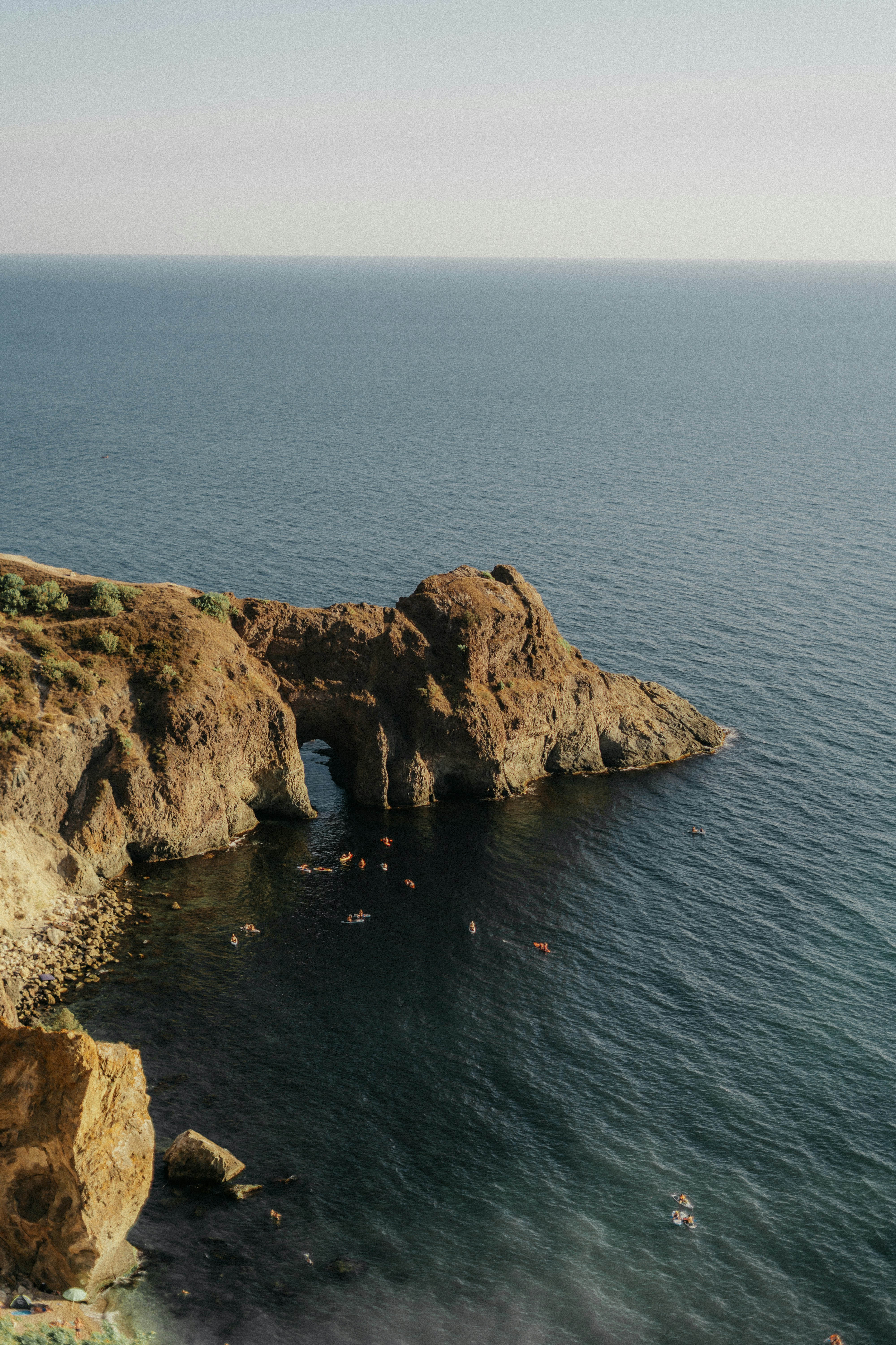 Kayakers explore a rocky archway on the coast.
