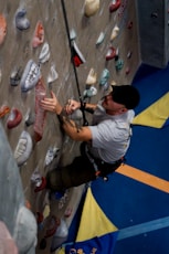 Man climbing indoor rock wall with safety rope
