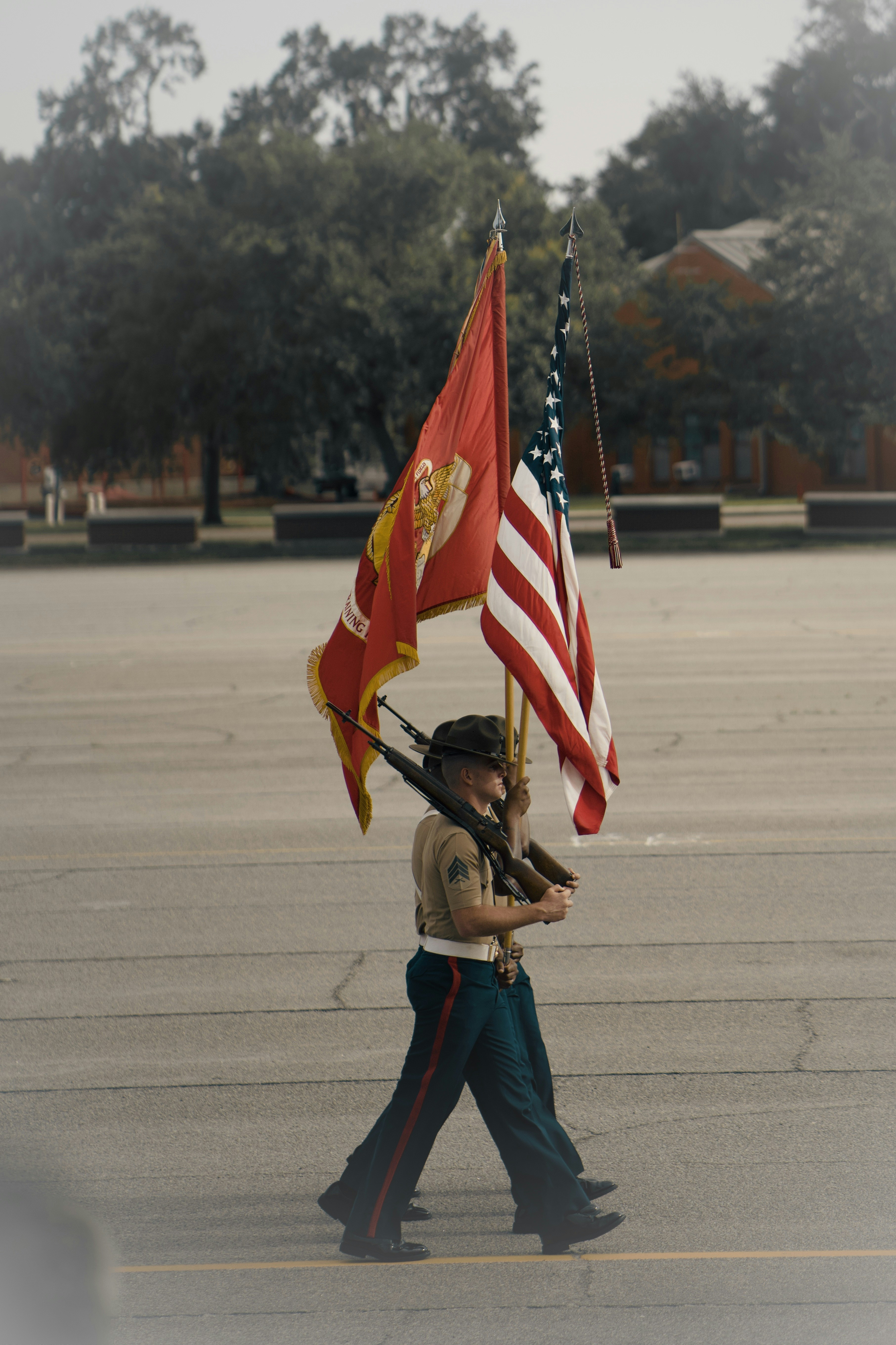 Marines in uniform march with flags and rifles.