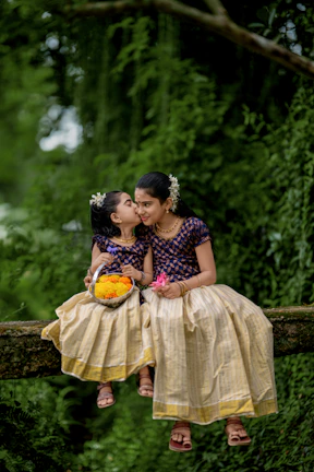Two young girls in traditional indian attire sitting on a branch.