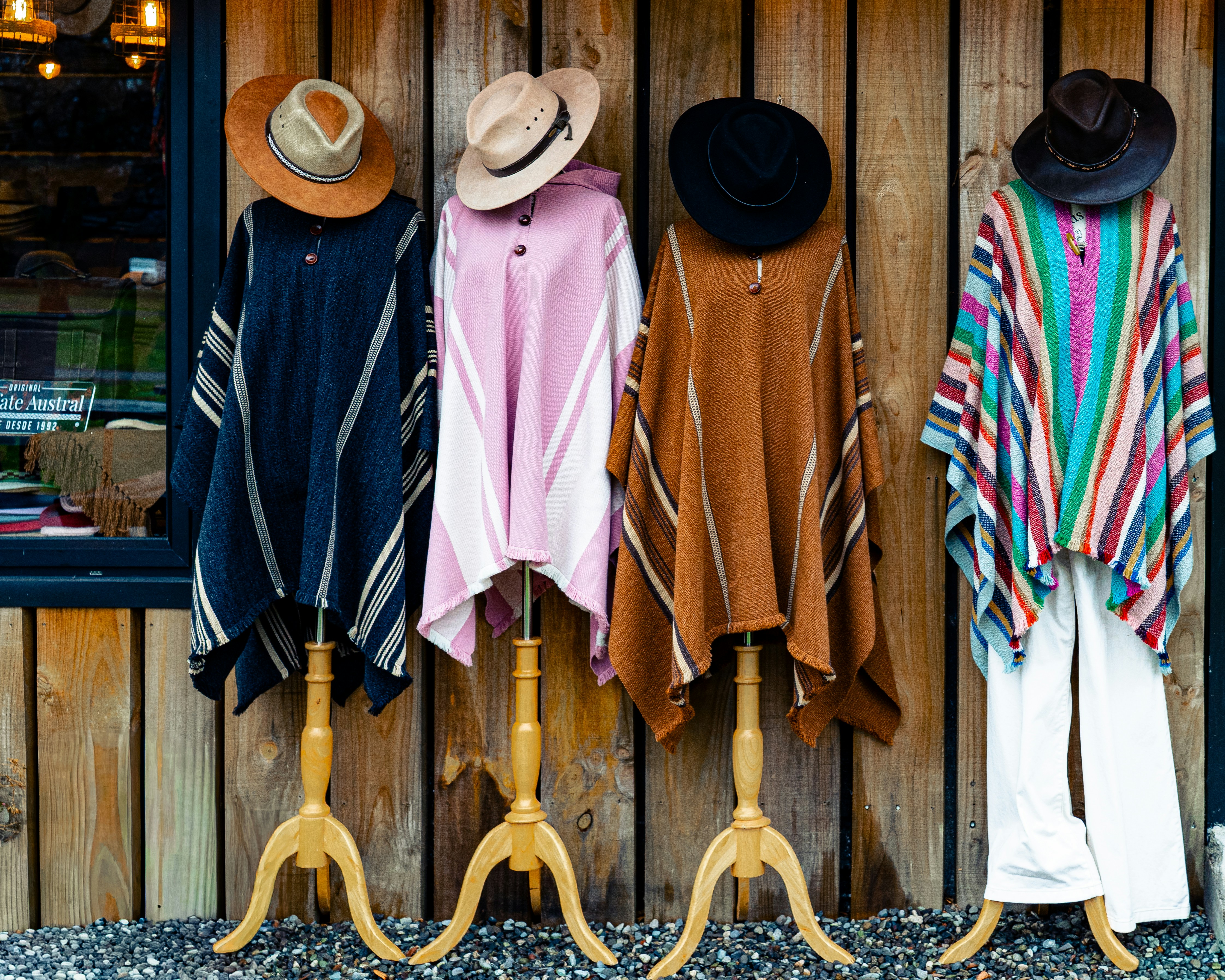 Four colorful ponchos displayed on mannequins outside.