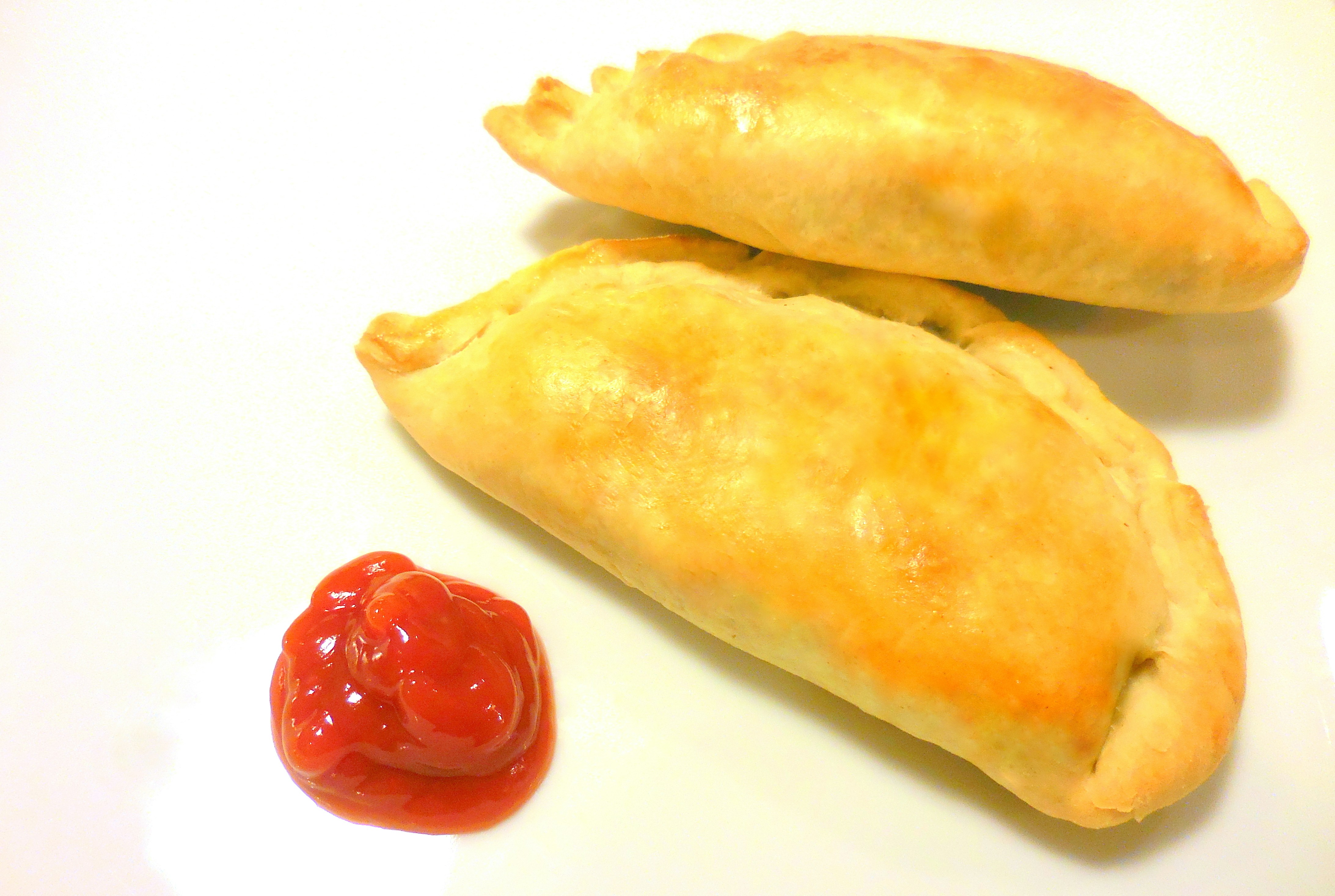 Two golden brown pastries with a dollop of ketchup.