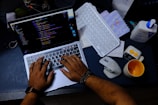 Hands typing on a laptop with code on screen.