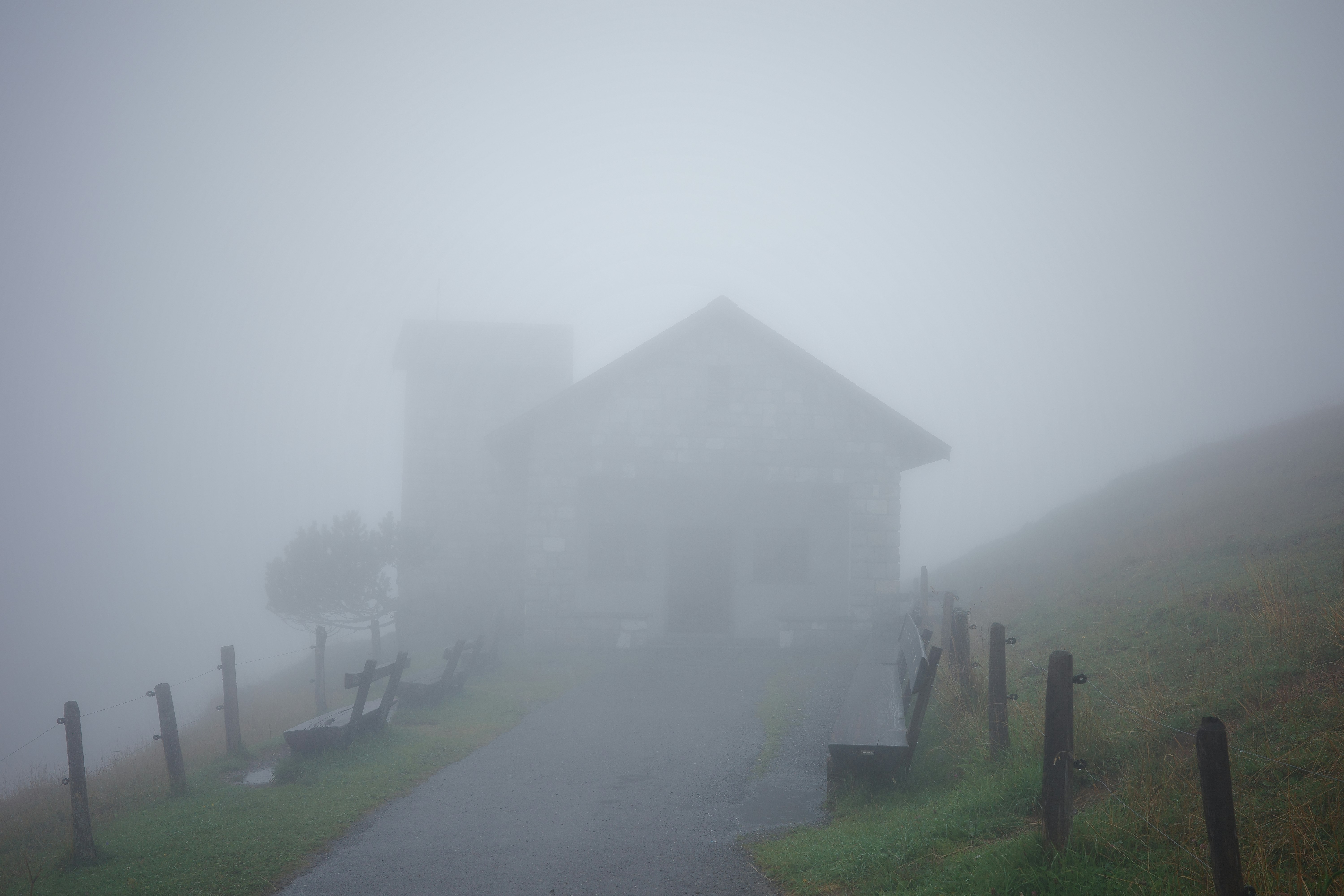 A building shrouded in thick fog on a grassy hill.