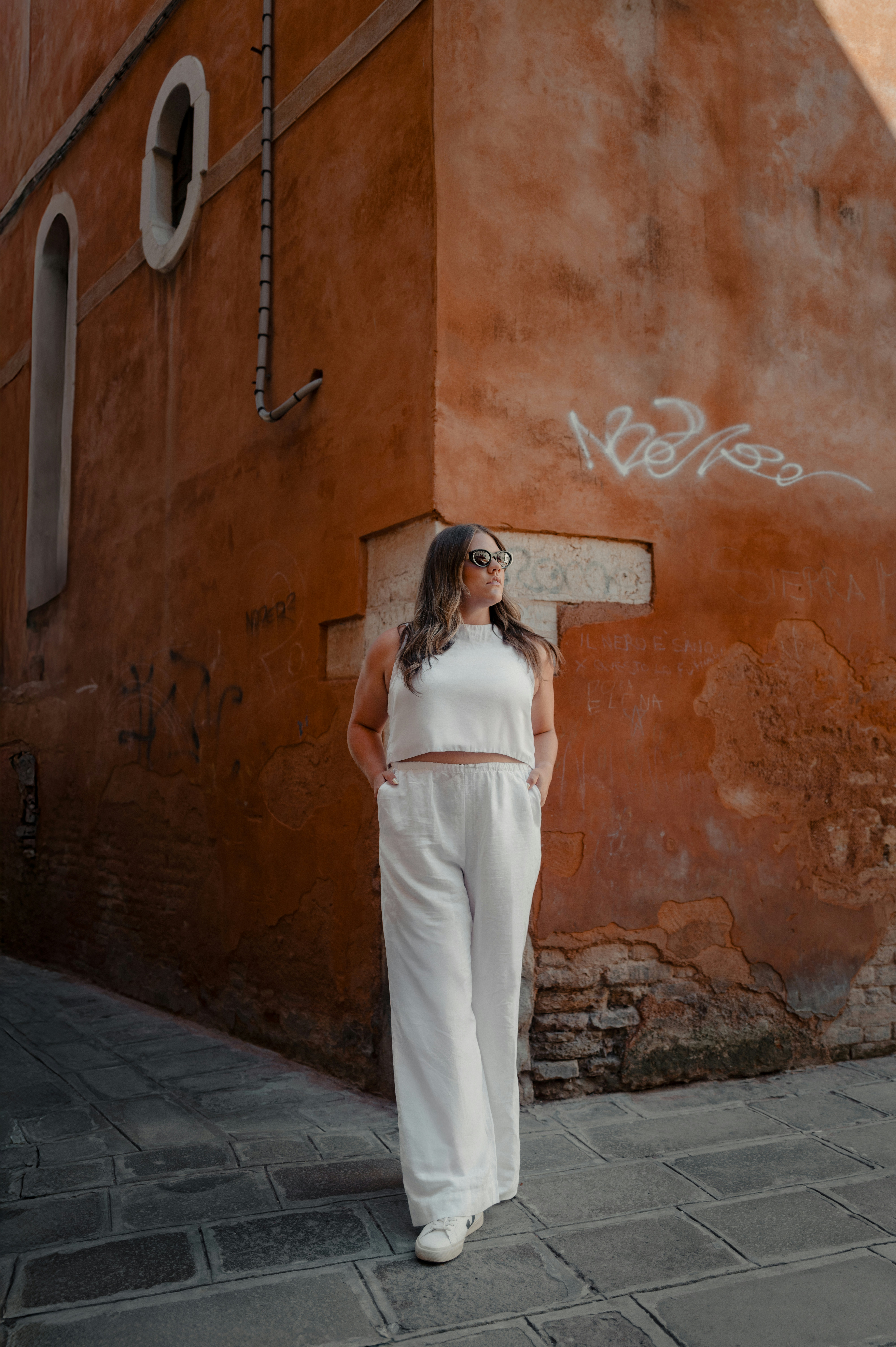 Woman in white outfit stands on cobblestone street.