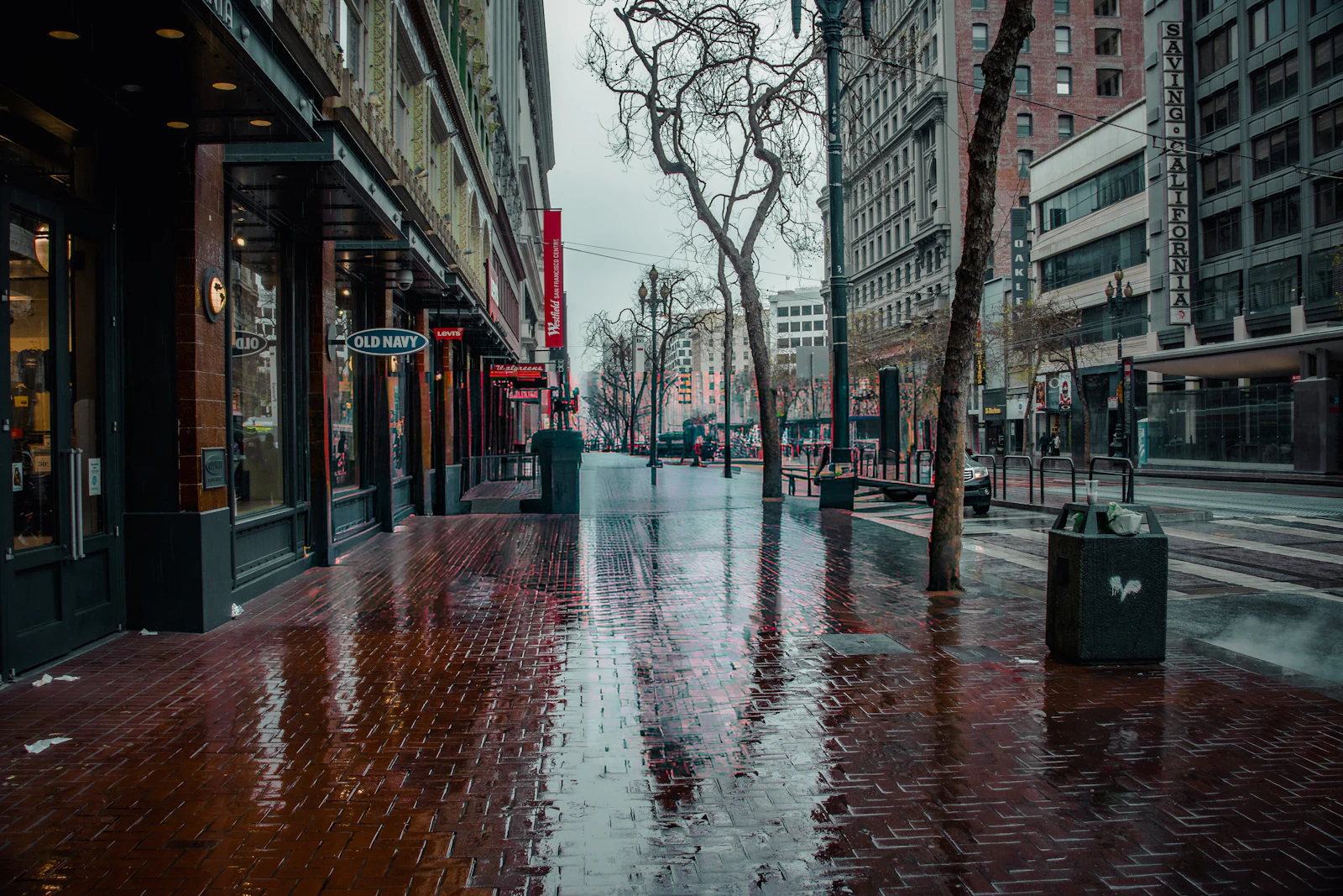 An empty city pavement reflects shop lights after rainfall.