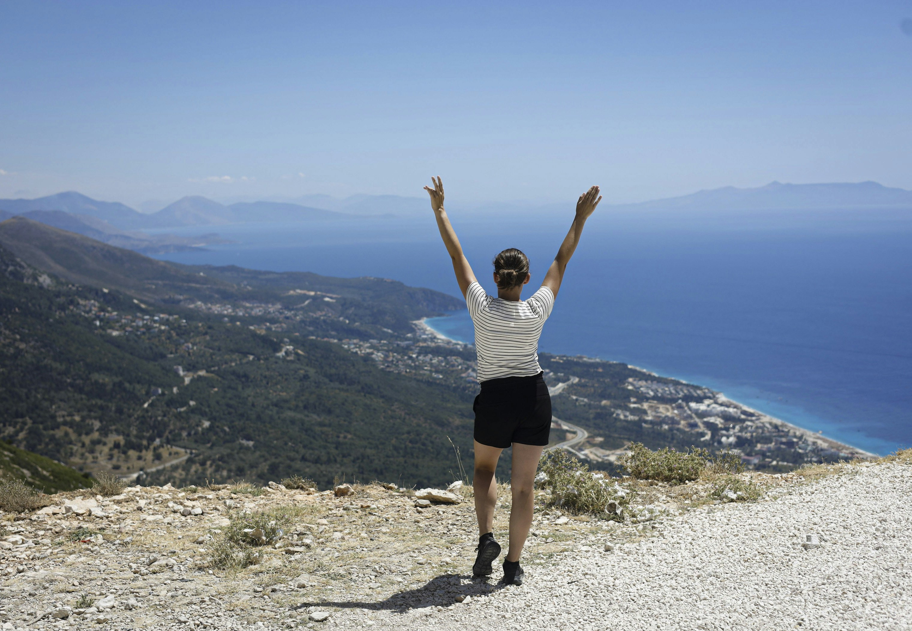 Woman with arms raised on a mountain overlooking the sea.