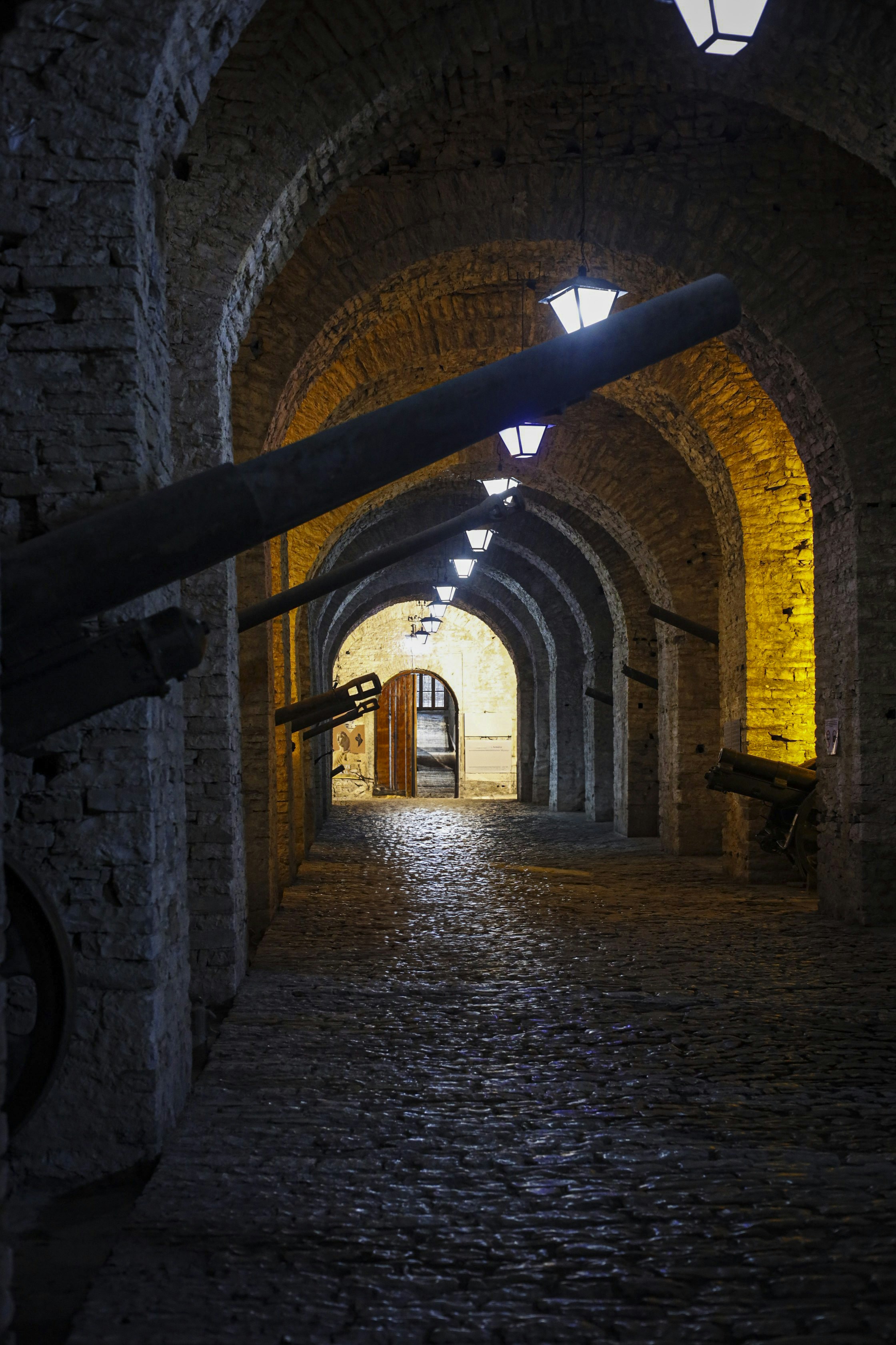 Dark stone arched corridor with cannons and lanterns