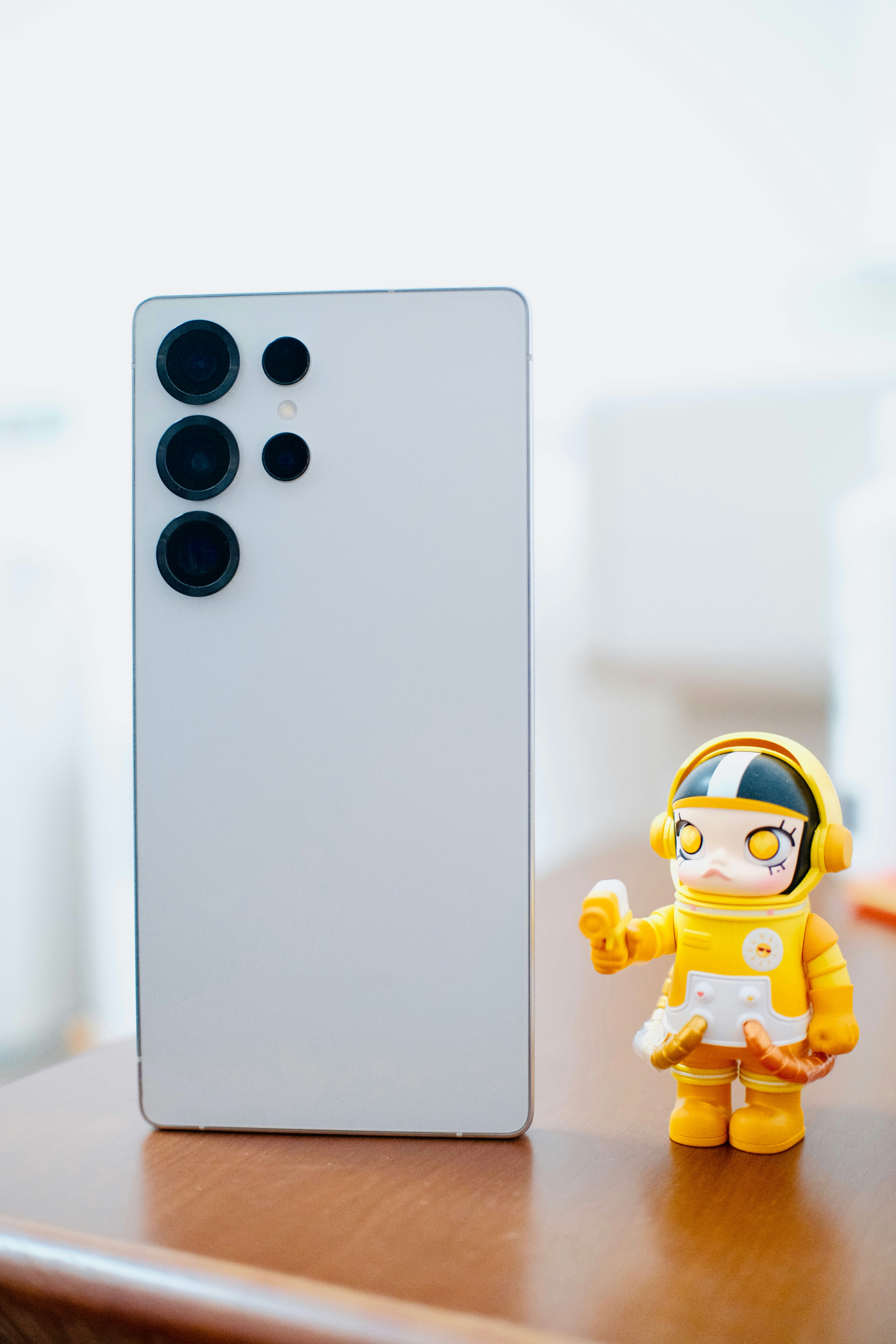 Weißes Smartphone und Astronautenspielzeug auf Holztisch.