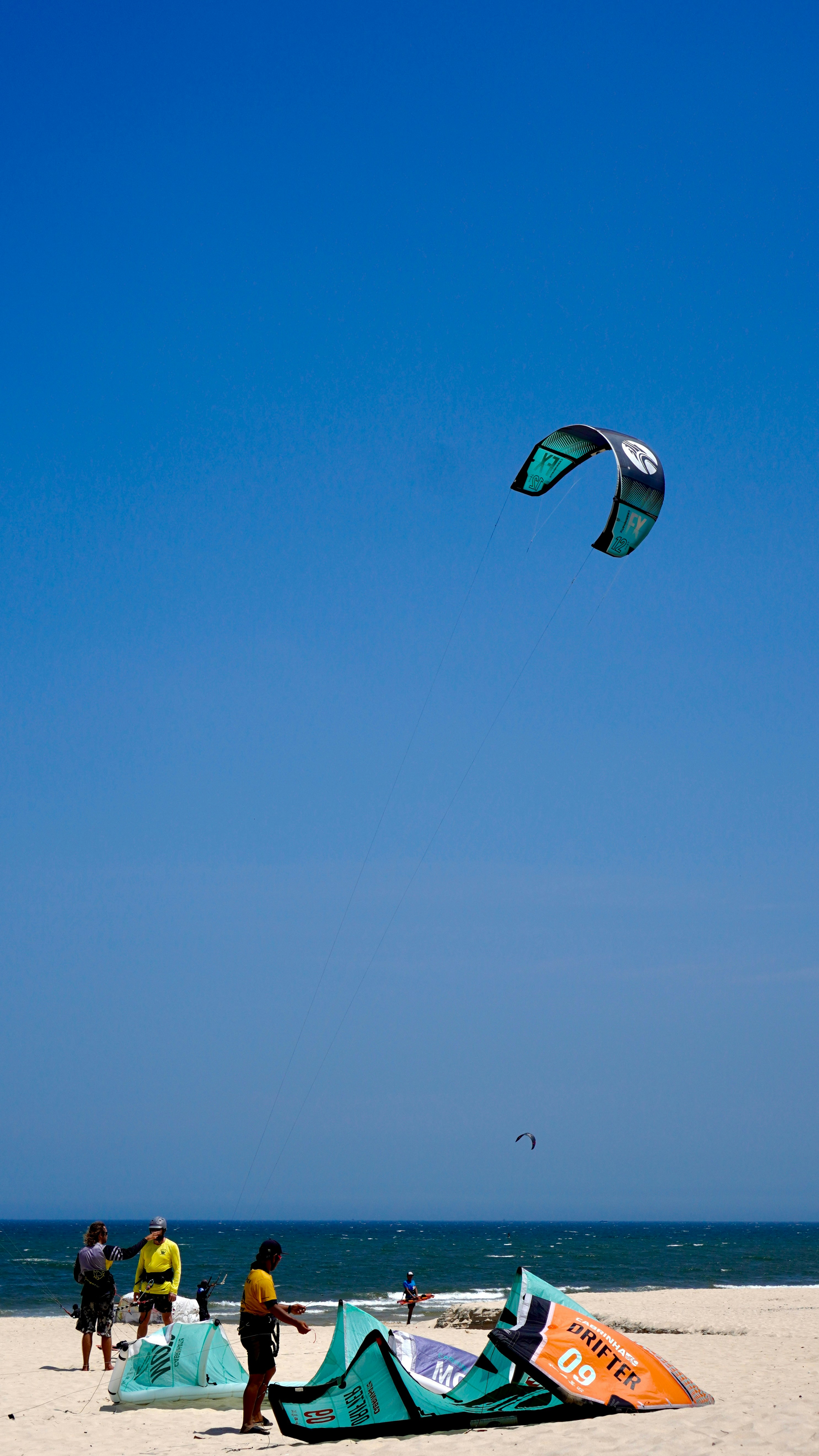 Kite surfers prepare on a sunny beach with clear skies.
