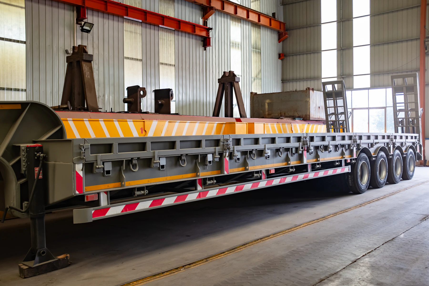 A multi-axle lowboy step-deck flatbed trailer with a low drop deck for tall, heavy open-deck loads