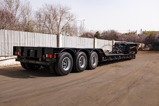 A black triple axle trailer parked on pavement.