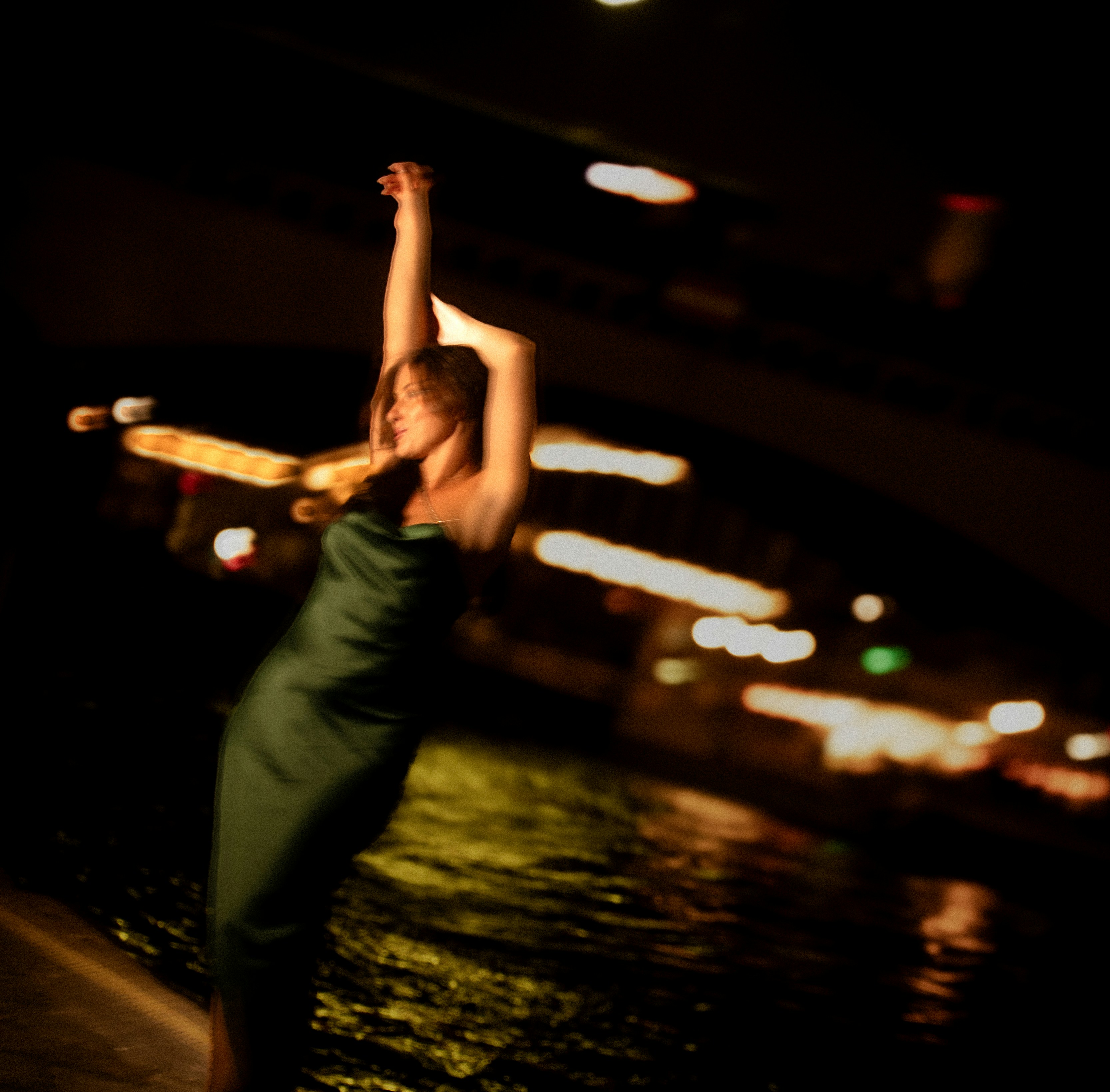 Mulher em um vestido verde dançando à beira da água à noite.