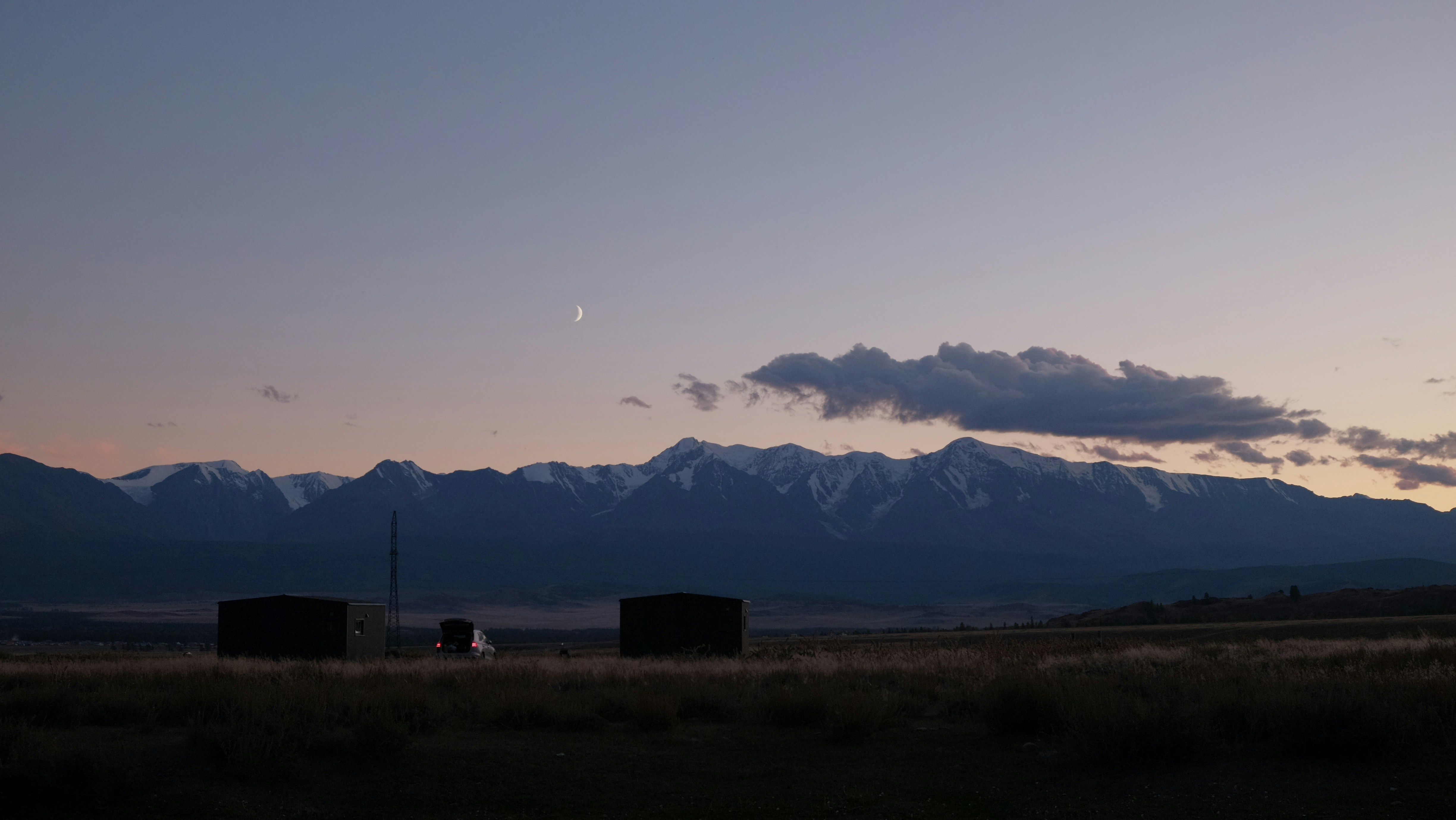 Dusk sky over snow-capped mountains and dark landscape.