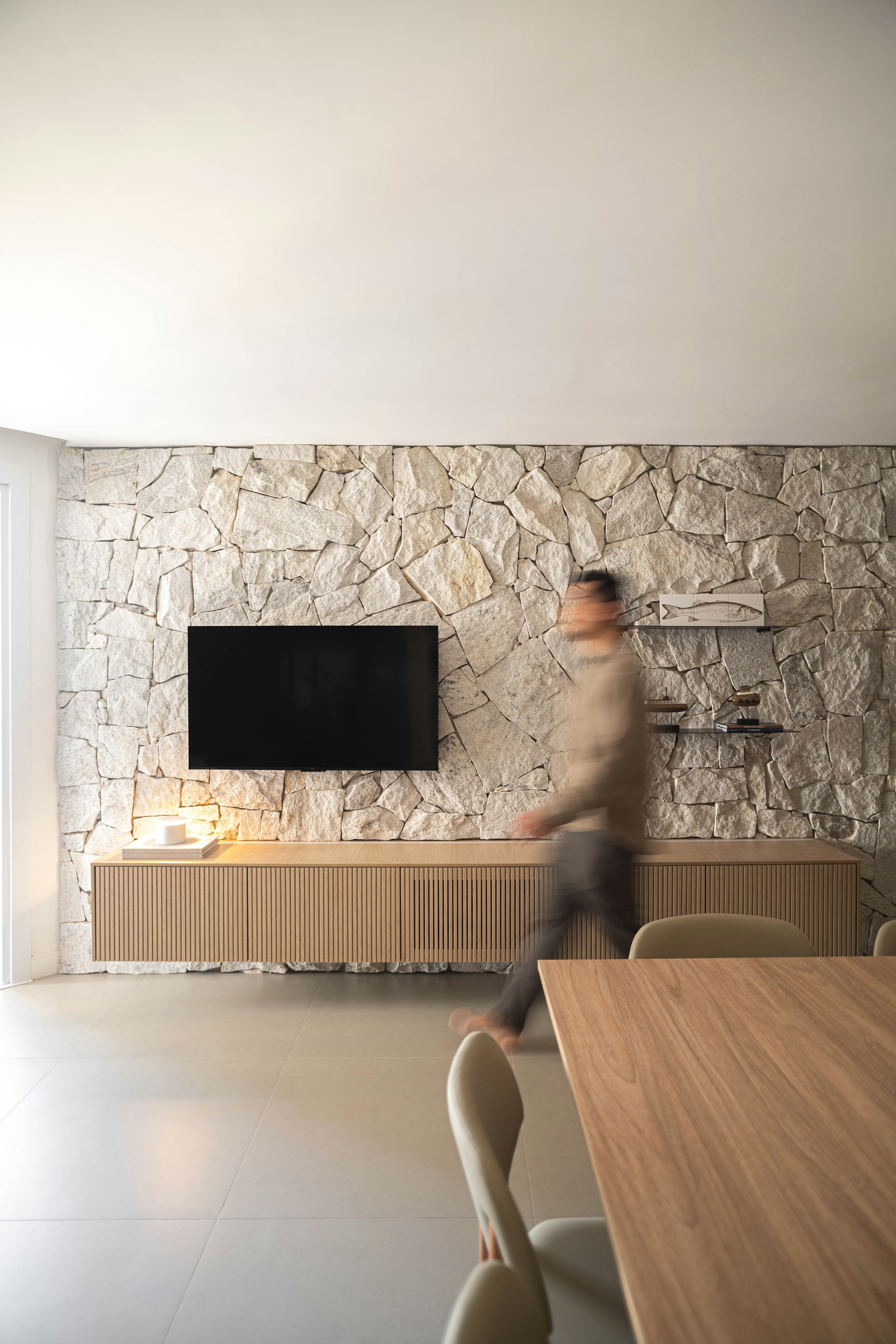 Man walking past a television on a stone wall
