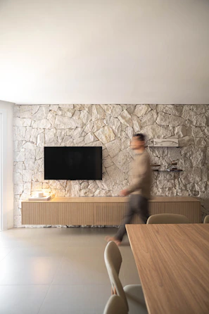 Man walking past a television on a stone wall