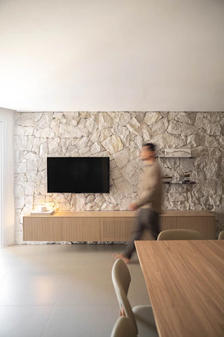 Man walking past a television on a stone wall