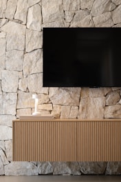 Modern television mounted on a stone wall above cabinet.