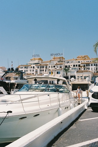 Boats docked at a sunny marina with buildings behind.