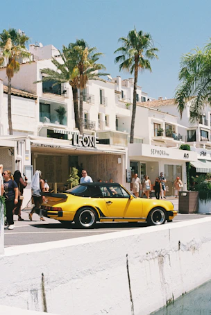 Yellow convertible car on a sunny street with palm trees.