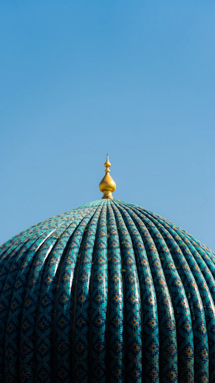 Turquoise dome with golden spire against blue sky