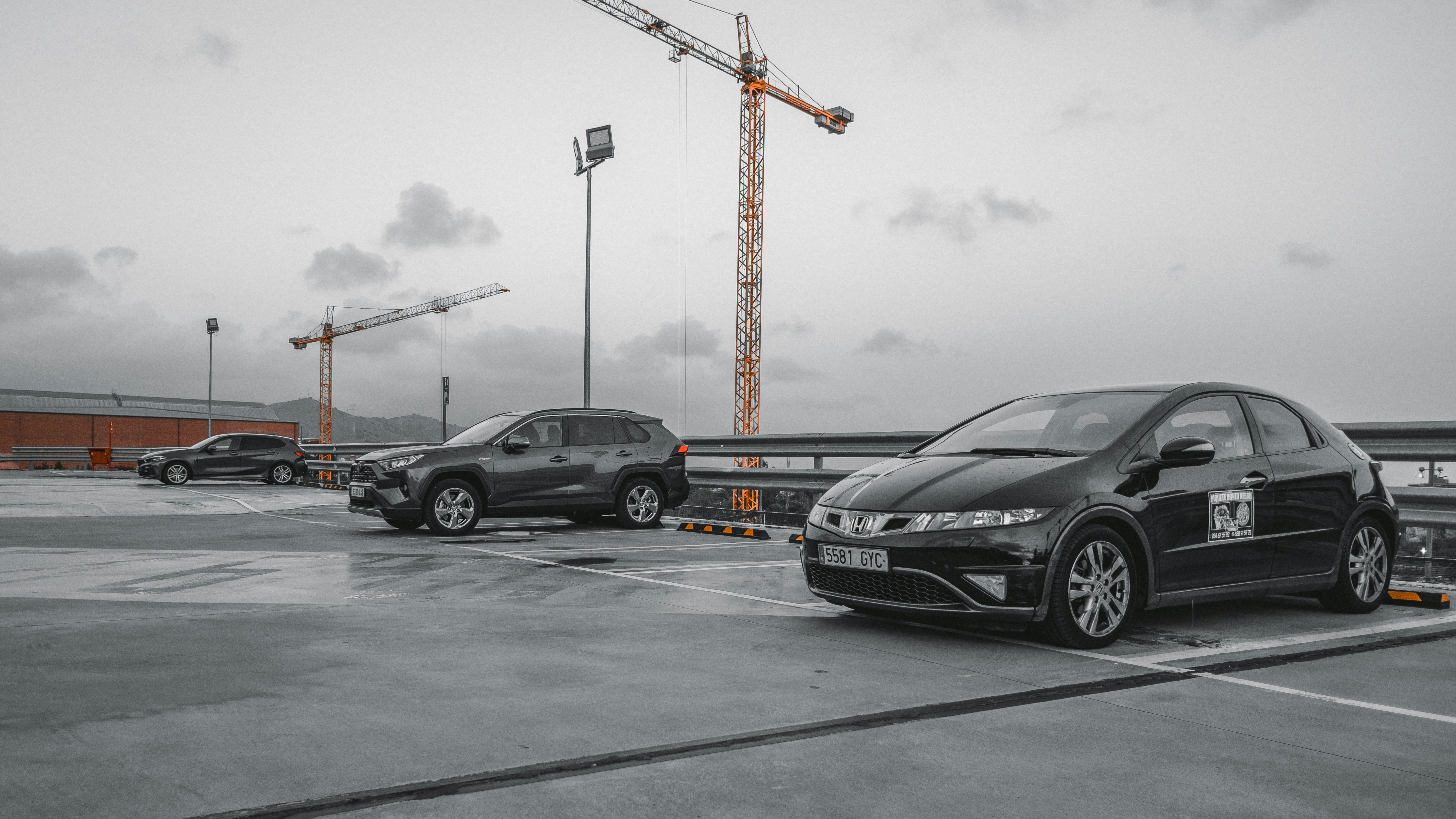 Cars parked on a rooftop with cranes in background.