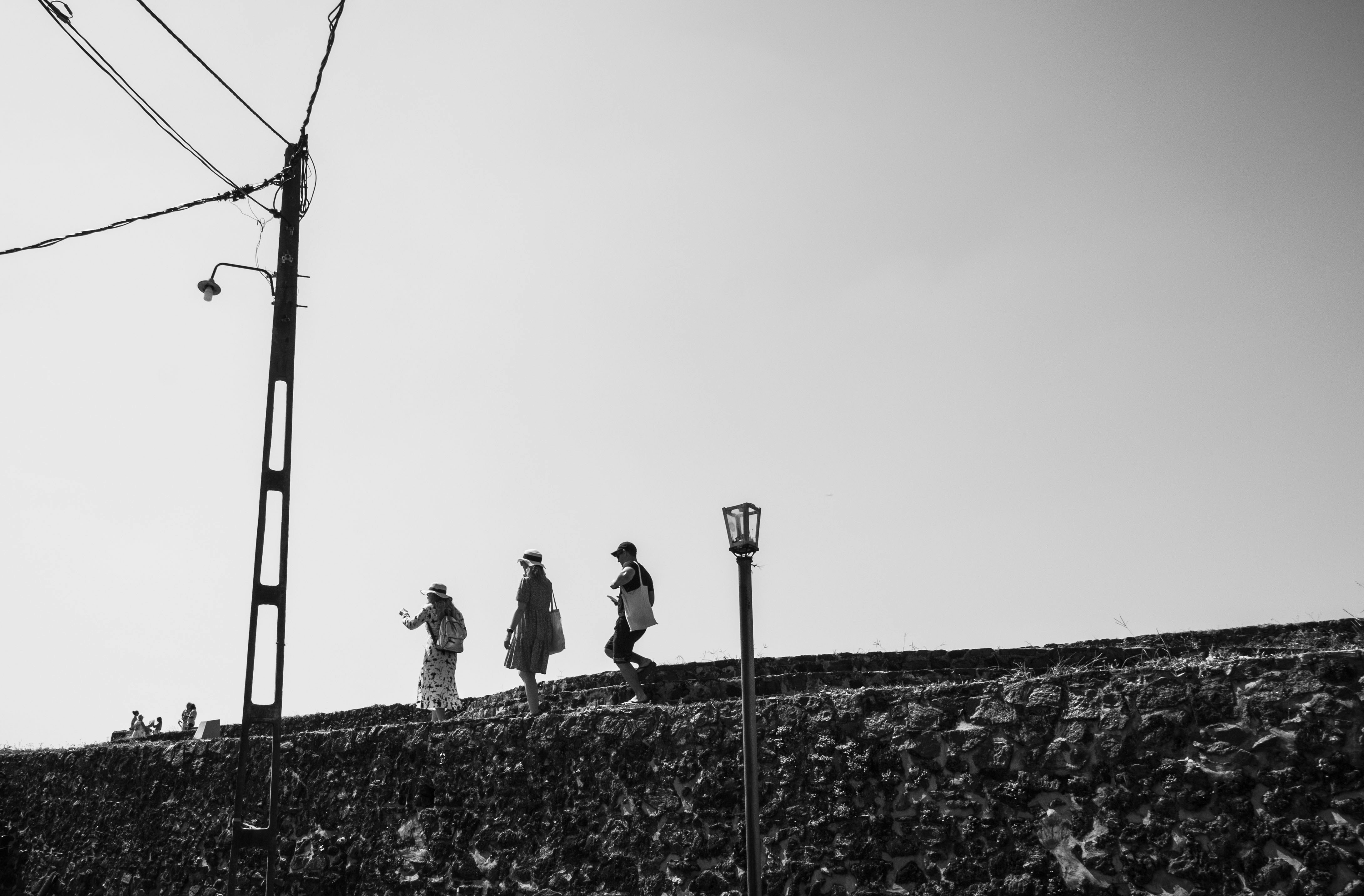 Tres figuras caminan a lo largo de una pared texturizada bajo el cielo.