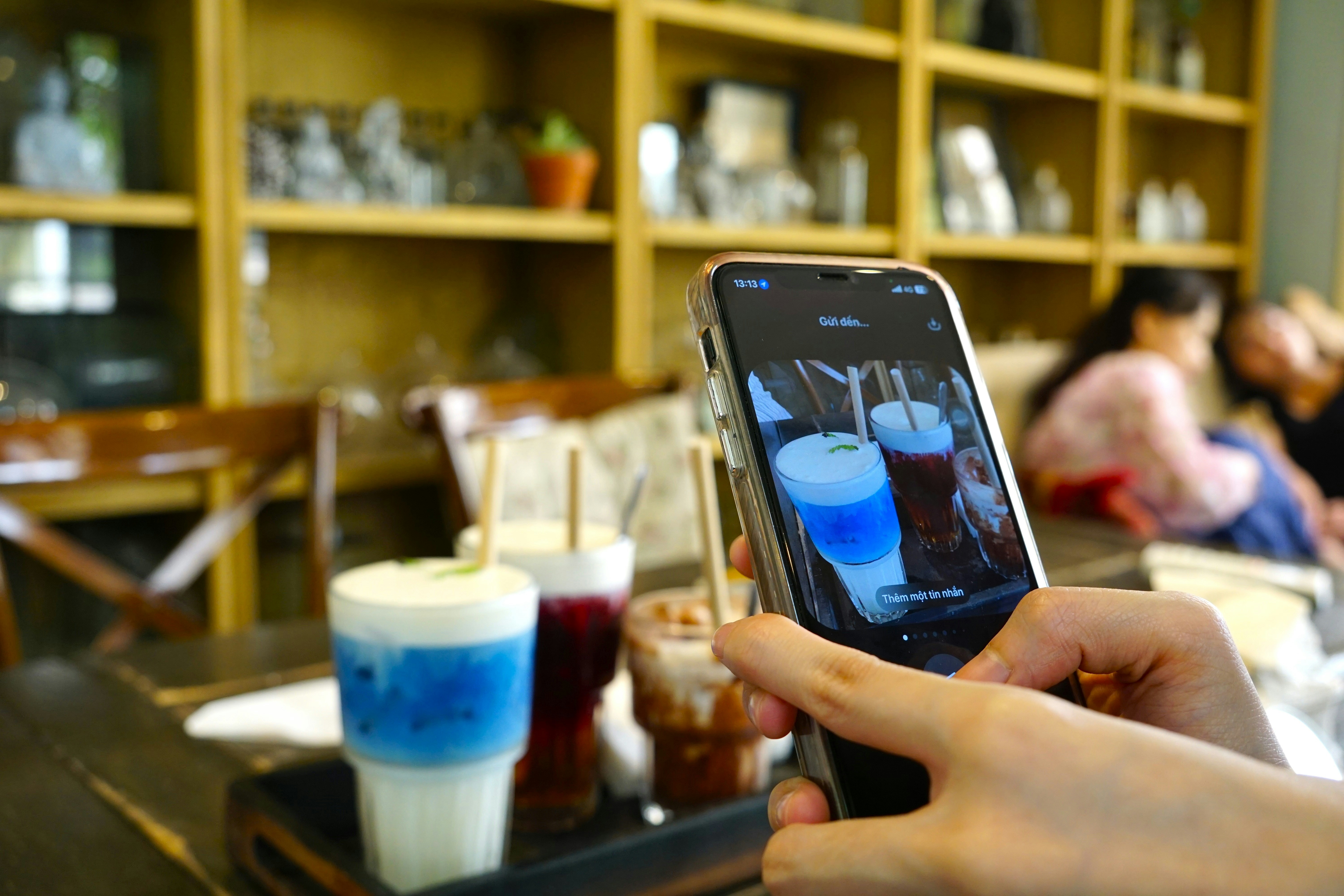 Seseorang merekam minuman berwarna di meja bar sebuah kedai menggunakan ponsel