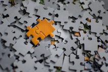 A single orange puzzle piece rests on a pile of grey pieces.