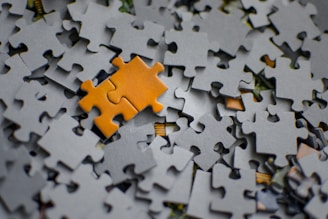 A single orange puzzle piece rests on a pile of grey pieces.