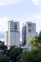 Two tall apartment buildings with trees in foreground.