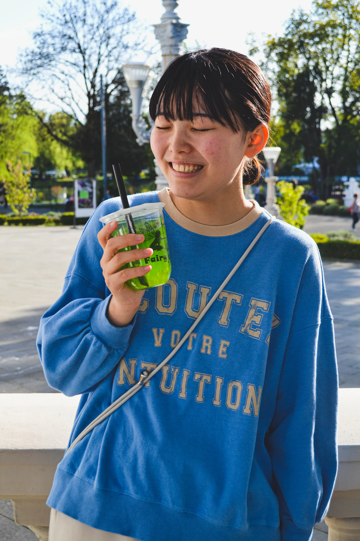 Young woman holding a bright green drink outdoors
