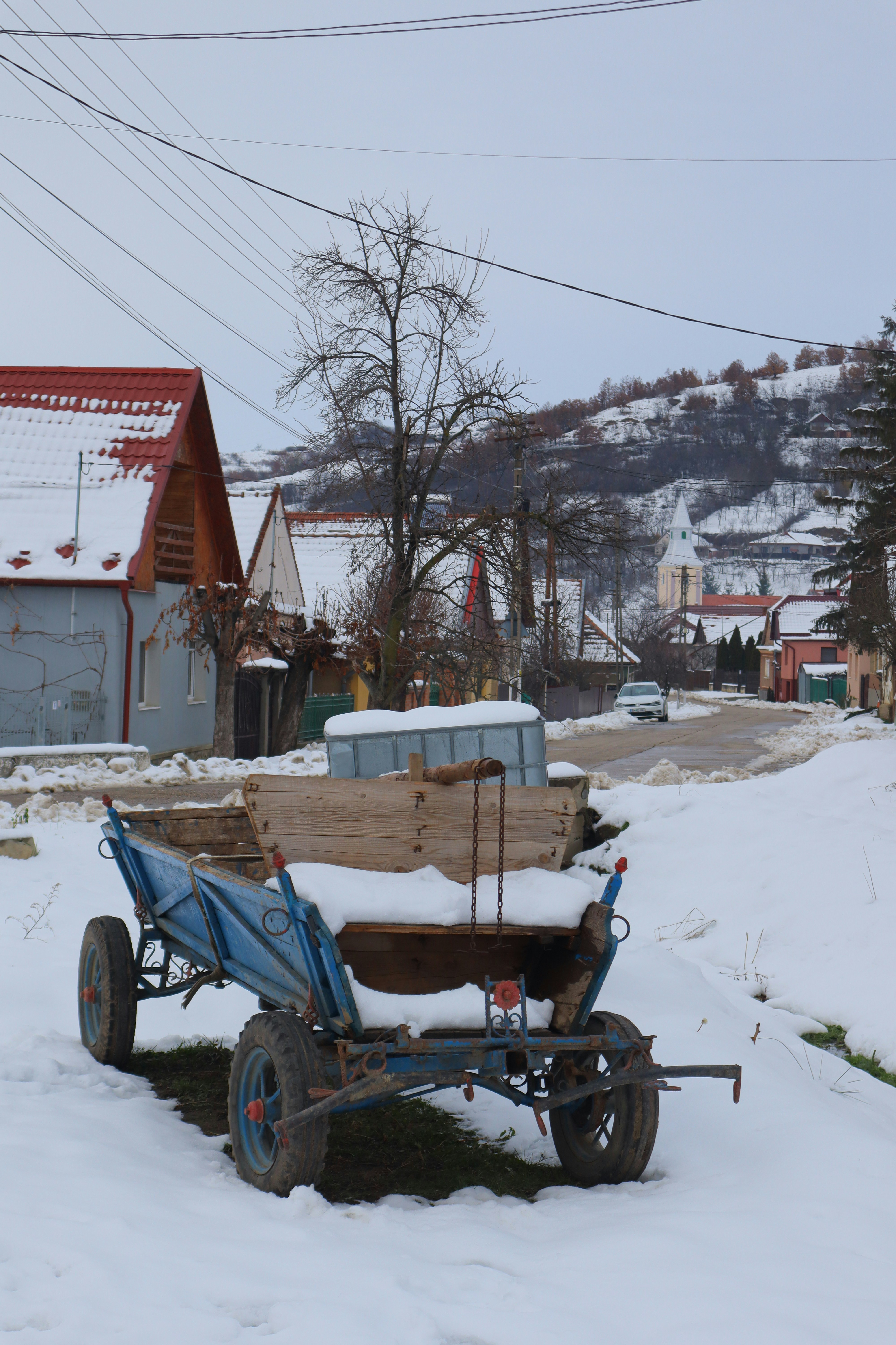 A blue cart sits in the snow near houses.