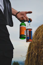 Person holding two bottles next to haystack