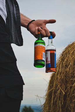 Person holding two bottles next to haystack