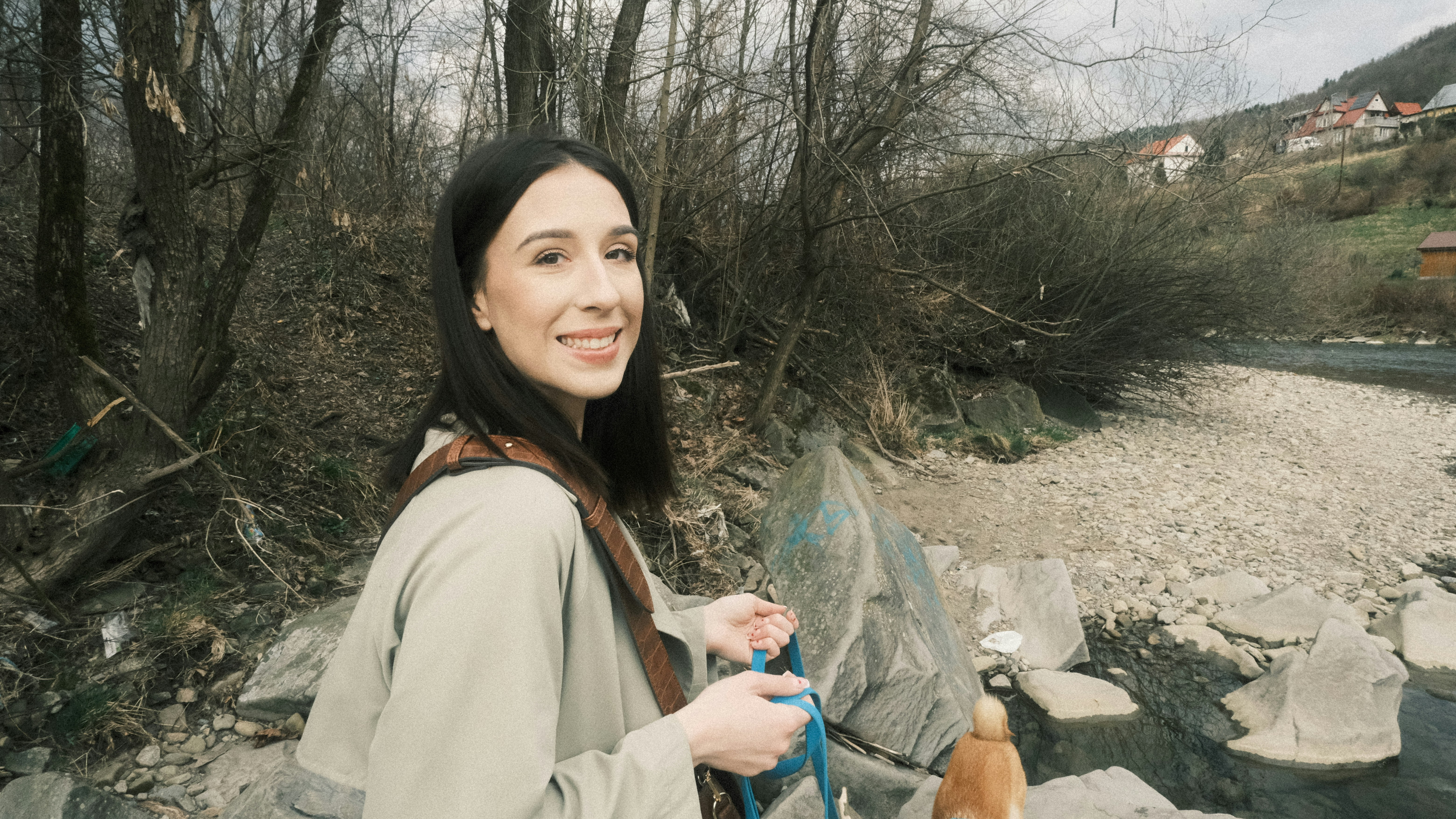 Eine Frau lächelt, während sie mit einem kleinen Hund im Freien spazieren geht.