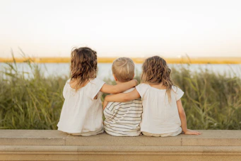 Three children sitting together looking at the water.