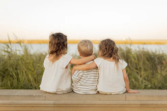 Three children sitting together looking at the water.