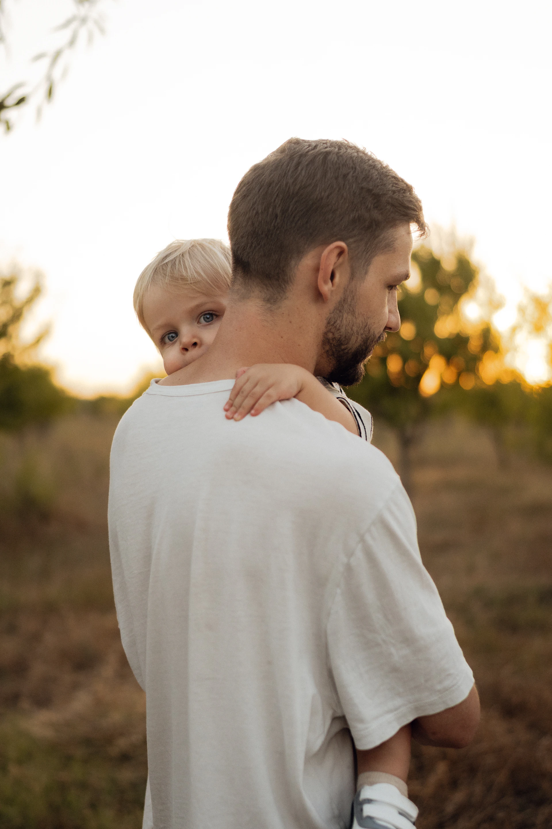 Father holds his young son over his shoulder outside.